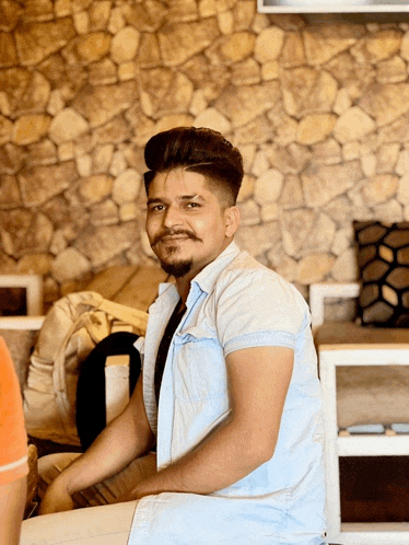 a young man with a beard is sitting on a couch in front of a stone wall