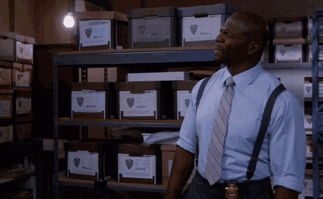 a man wearing suspenders and a tie stands in front of a shelf full of boxes with a new york city police badge