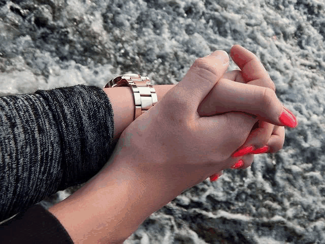 a woman with red nails and a watch on her wrist holds another woman 's hand