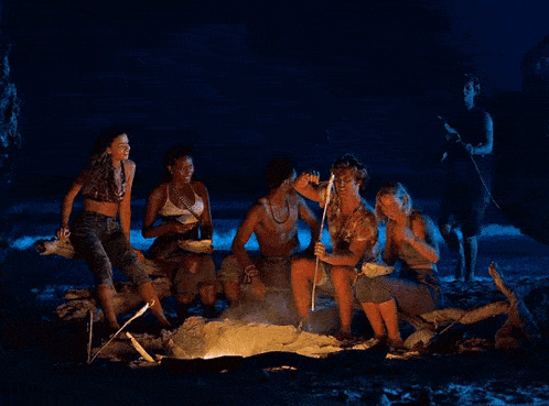 a group of people are sitting around a campfire on the beach at night