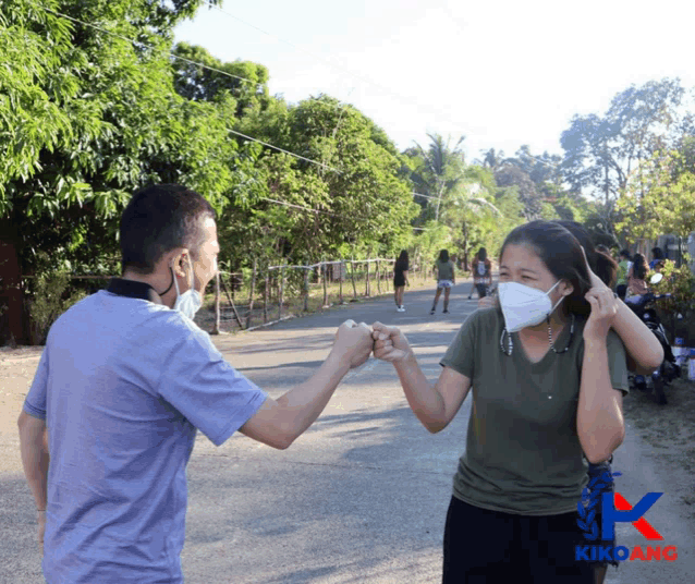 a man and a woman wearing face masks are giving each other a fist bump in front of a kikoano logo