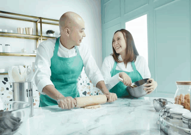 a man and a woman in green aprons are rolling dough