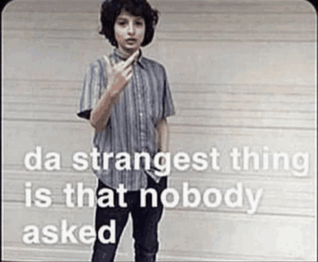 a young boy is giving the middle finger in front of a garage door with the words `` da strangest thing is that nobody asked '' .