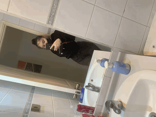 a woman taking a picture of herself in a bathroom mirror with a bottle of shampoo on the counter