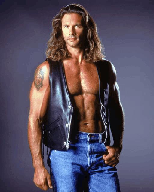 a man with long hair and a tattoo on his arm is wearing a leather vest and jeans