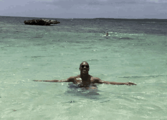 a man in sunglasses is swimming in the ocean with his arms outstretched