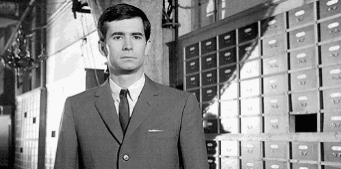 a black and white photo of a man in a suit and tie standing in front of a row of safes .