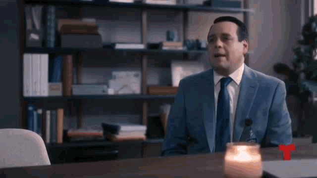 a man in a suit and tie is sitting at a desk with a candle in front of him .