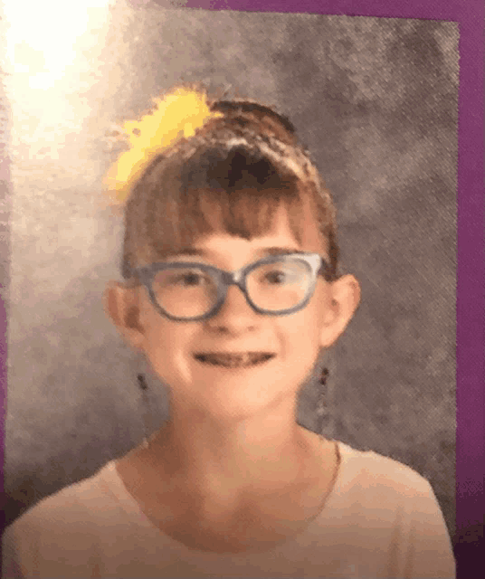 a young girl wearing glasses and a yellow bow in her hair