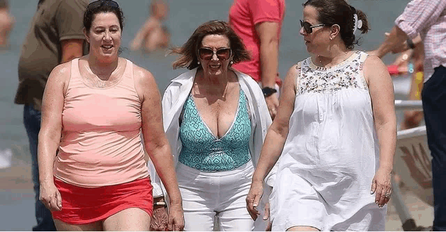 three women are walking on a beach and one of them is wearing a swimsuit .