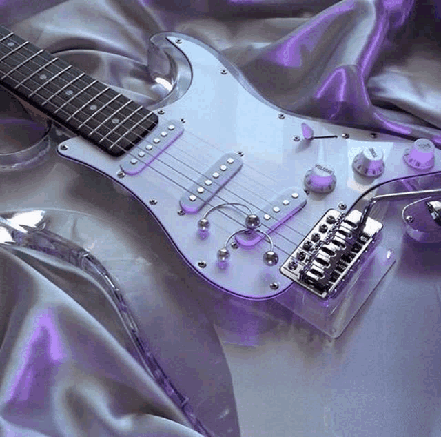 a clear electric guitar is laying on a purple satin cloth