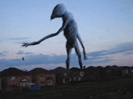 a statue of a giant alien standing in a field in front of a house .