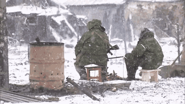 two soldiers are sitting in the snow near a barrel and a sign that says ' crakob ' on it