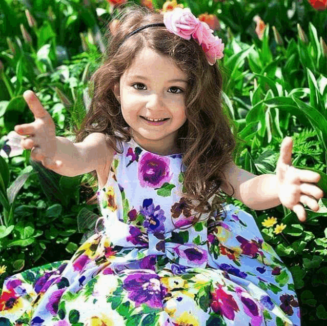 a little girl in a floral dress is sitting in a field of flowers with her arms outstretched