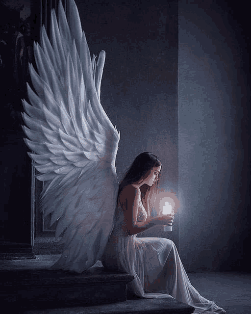 a woman with angel wings is sitting on a staircase holding a candle