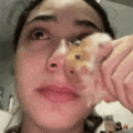 a woman is holding a hamster in front of her face and looking at it .