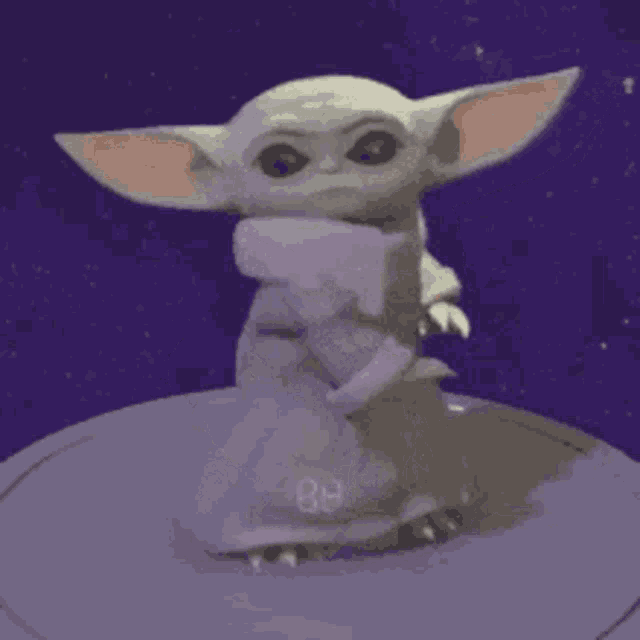 a baby yoda from the mandalorian is standing on a purple surface .