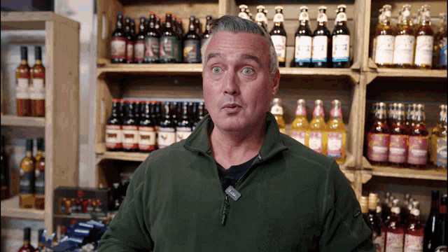 a man stands in front of a shelf full of bottles of alcohol including one that says ' strawberry '