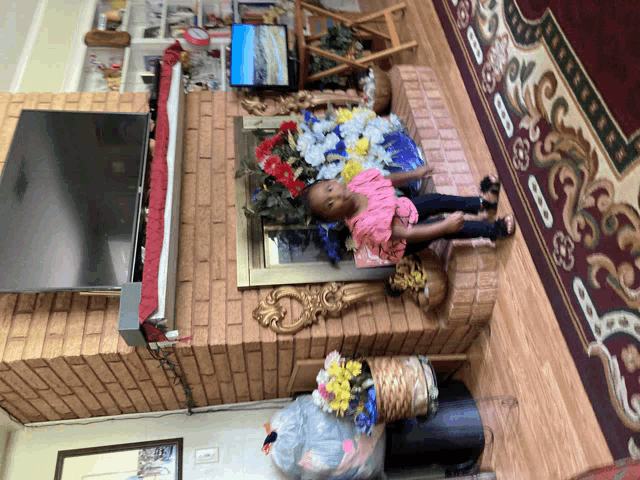 a little girl laying on a brick fireplace in front of a flat screen tv