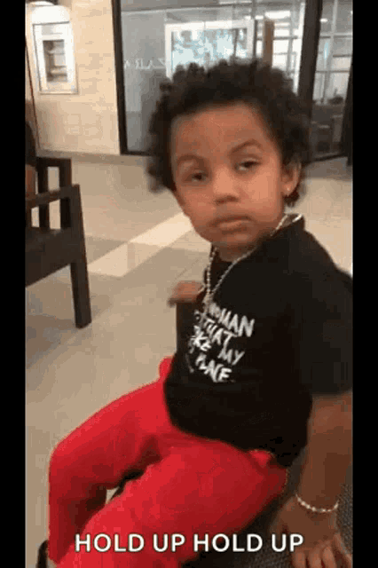 a young boy wearing a black shirt and red pants is sitting on a chair in a waiting room .