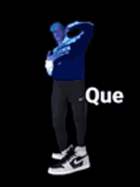 a man in a blue sweater and black pants is standing in front of a black background with the word que written on it .