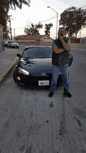 a man is standing in front of a black car on a street .