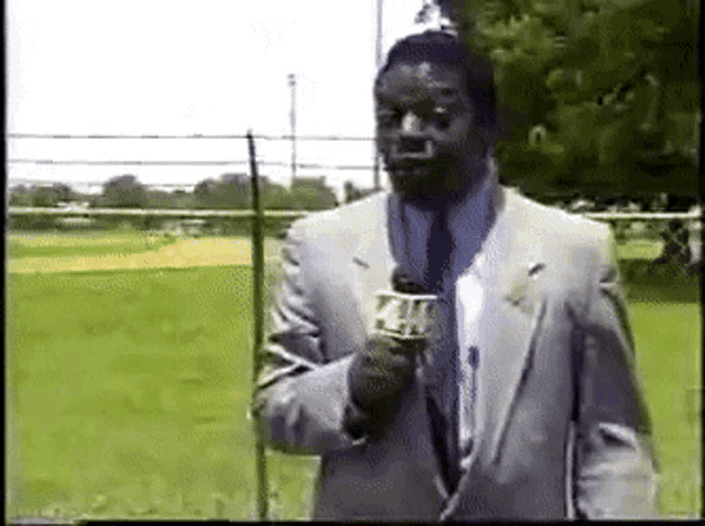 a man in a suit and tie is holding a microphone in front of a field ..