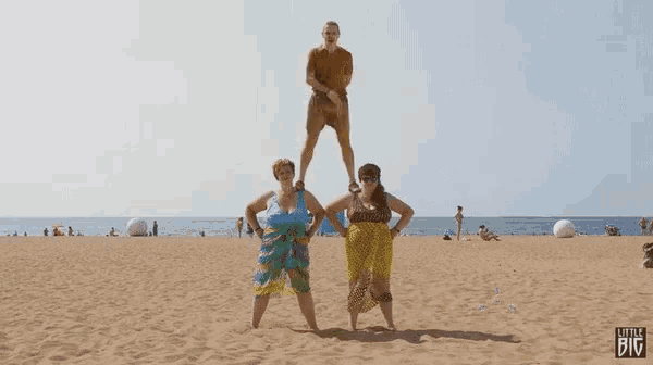 a man stands on top of two women on a sandy beach with the words little big on the bottom right