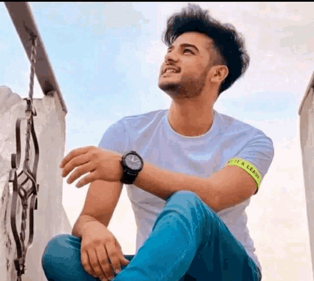 a young man is sitting on a balcony wearing a watch and a yellow band around his wrist .