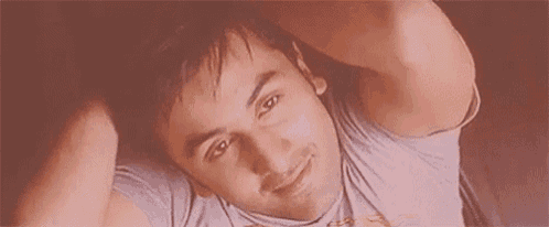 a young man is laying on a bed with his hands behind his head and smiling .