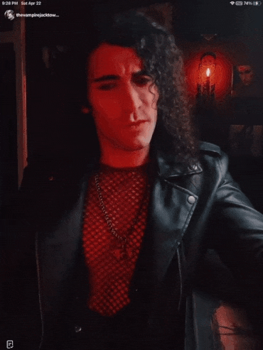 a man with long curly hair is wearing a black leather jacket and a red shirt