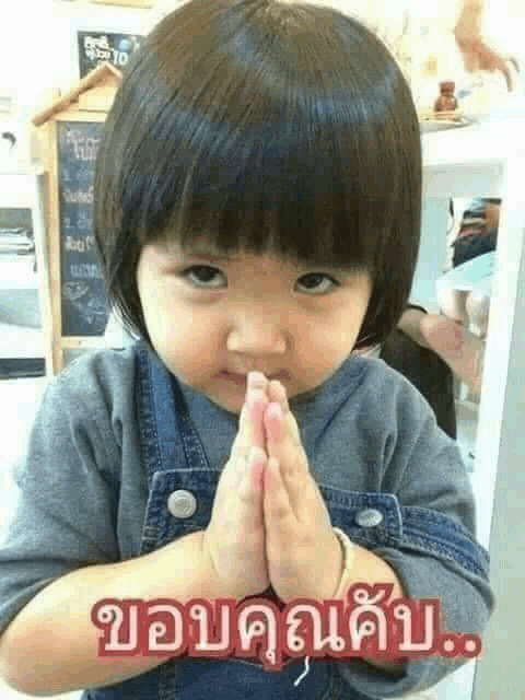 a little girl is making a face with her hands folded in prayer .