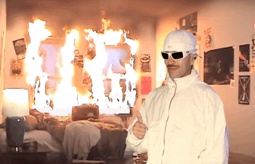 a man giving a thumbs up in front of a room that is on fire