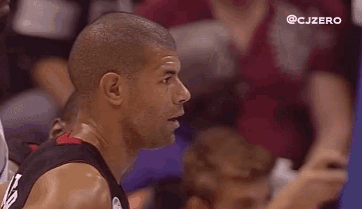 a group of men are sitting in a stadium watching a basketball game and one of them is looking at the camera .