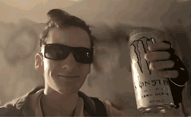 a man wearing sunglasses holds up a can of monster energy drink