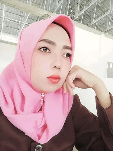 a woman wearing a pink hijab and a brown shirt