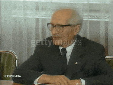 a man in a suit and tie is sitting at a table with the words getty images on the bottom right