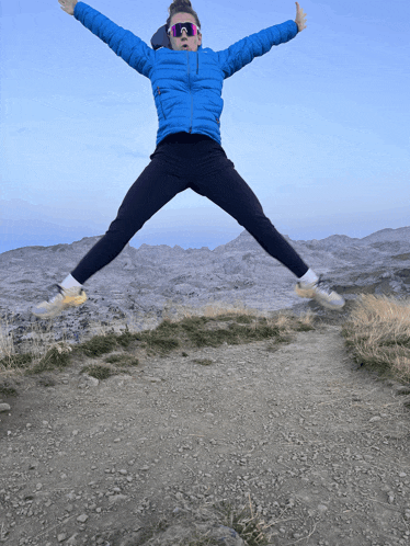 a person wearing a blue jacket and sunglasses is jumping in the air