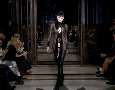 a model walks down the runway at a fashion show wearing a black jumpsuit with the word dogs written on it