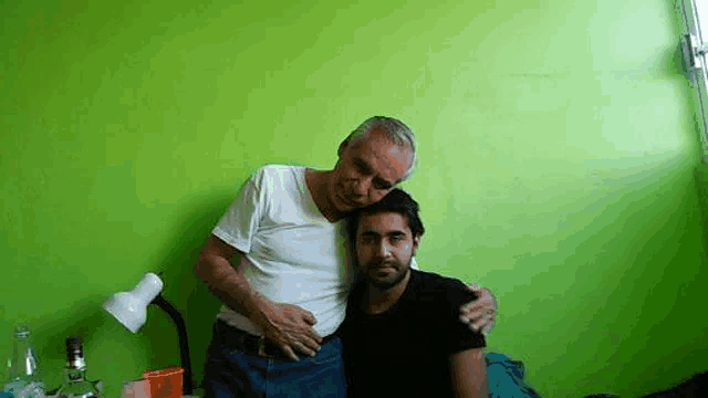 a man is hugging another man in a room with a green wall .