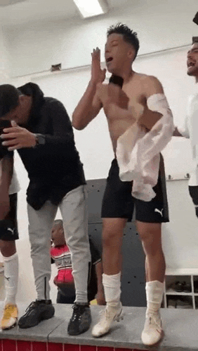 a group of men are standing in a locker room . one of the men is without a shirt on .