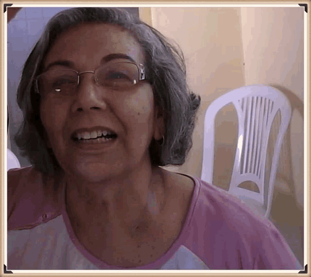 a woman wearing glasses and a pink shirt smiles in front of a white plastic chair