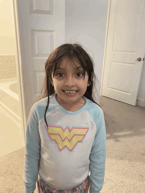 a little girl wearing a wonder woman shirt is smiling