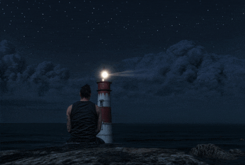 a man sits in front of a lighthouse that is lit up