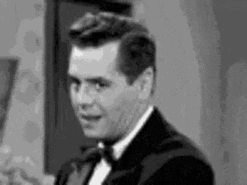 a man in a tuxedo and tie is making a funny face .