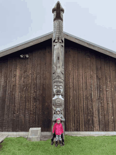 two children standing in front of a totem pole that says ' a ' on it