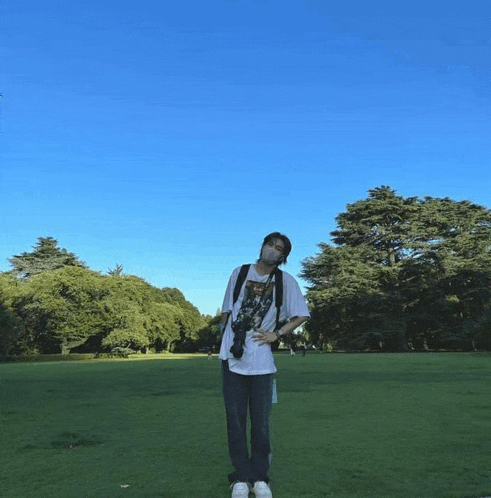 a man wearing a mask stands in a grassy field with trees in the background