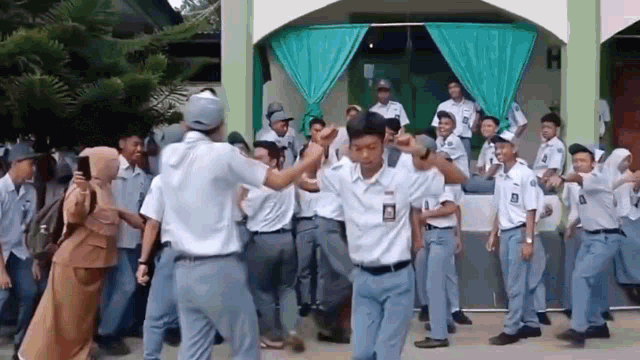 a group of boys in school uniforms are dancing in front of a building with the letter h on it