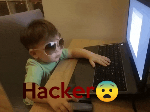 a little boy wearing sunglasses sits in front of a laptop with the word hacker written in red