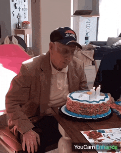 an older man wearing a buffalo bills hat sits at a table with a cake